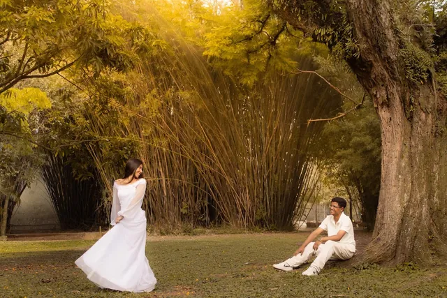 Noiva rodopiando de vestido branco e noivo sentado sob uma árvore em um bosque de bambu
